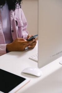 woman texting on smartphone at table with computer